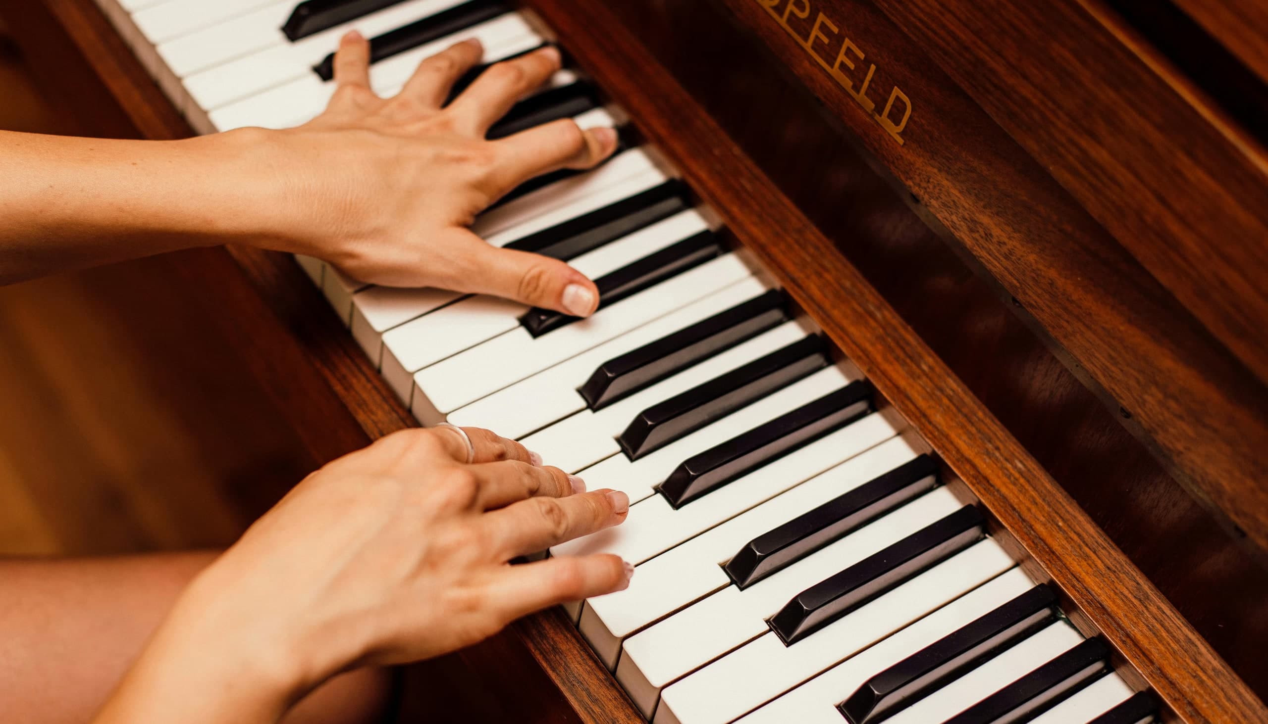 Two hands playing an upright piano